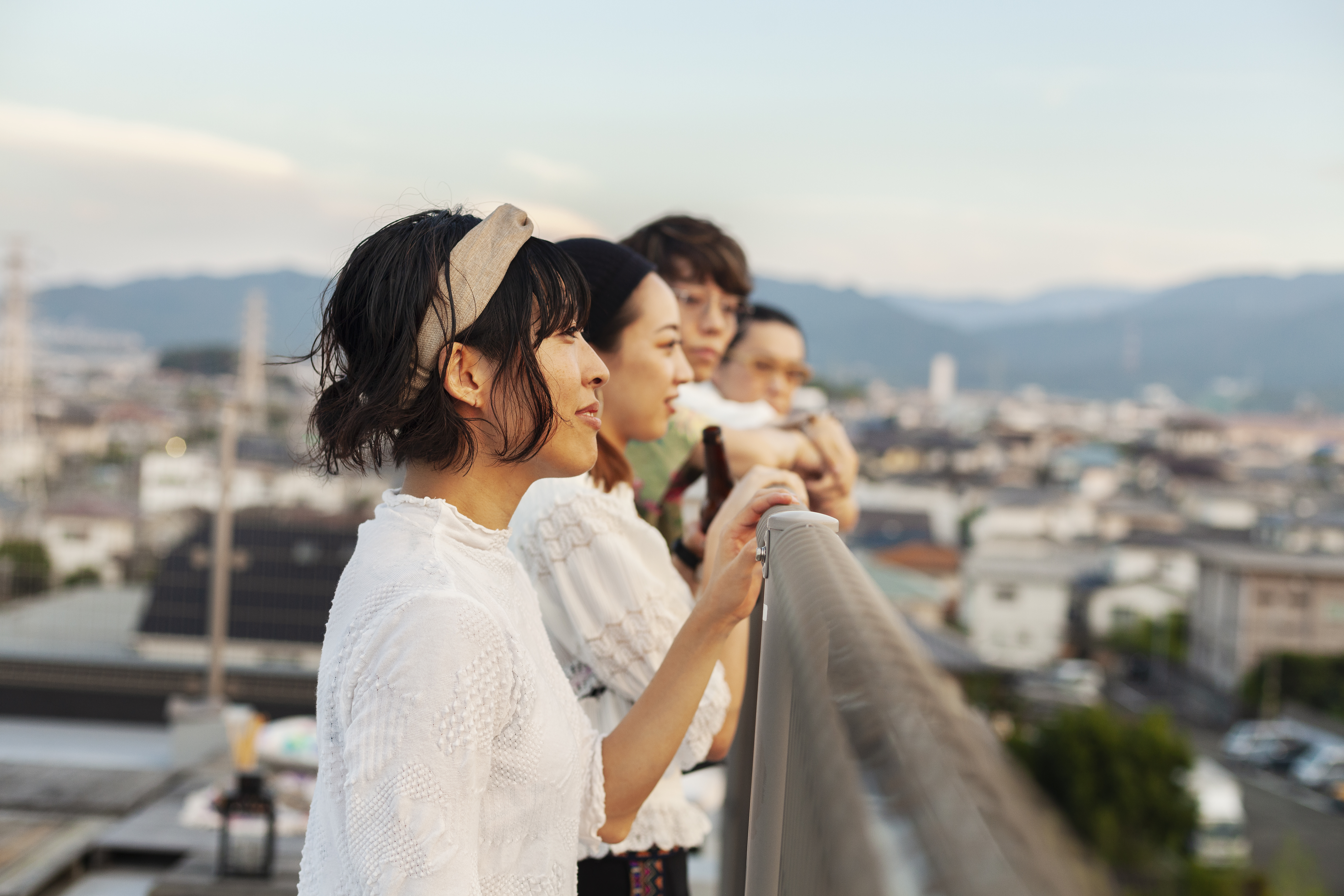 Group of young Japanese men and women standing on a rooftop in an urban setting.